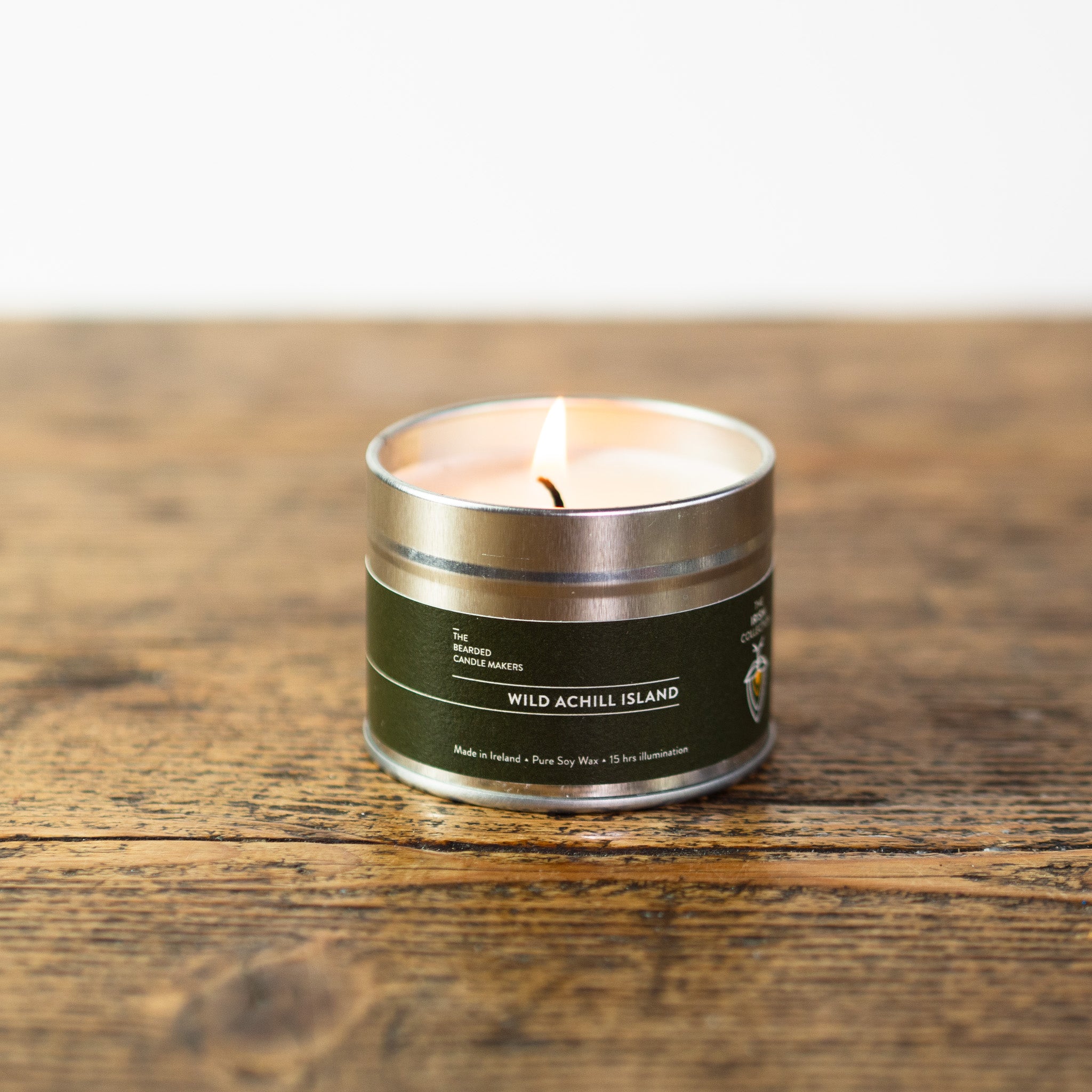 A photo of a lit tin candle, called Wild Achill Island on a wooden table
