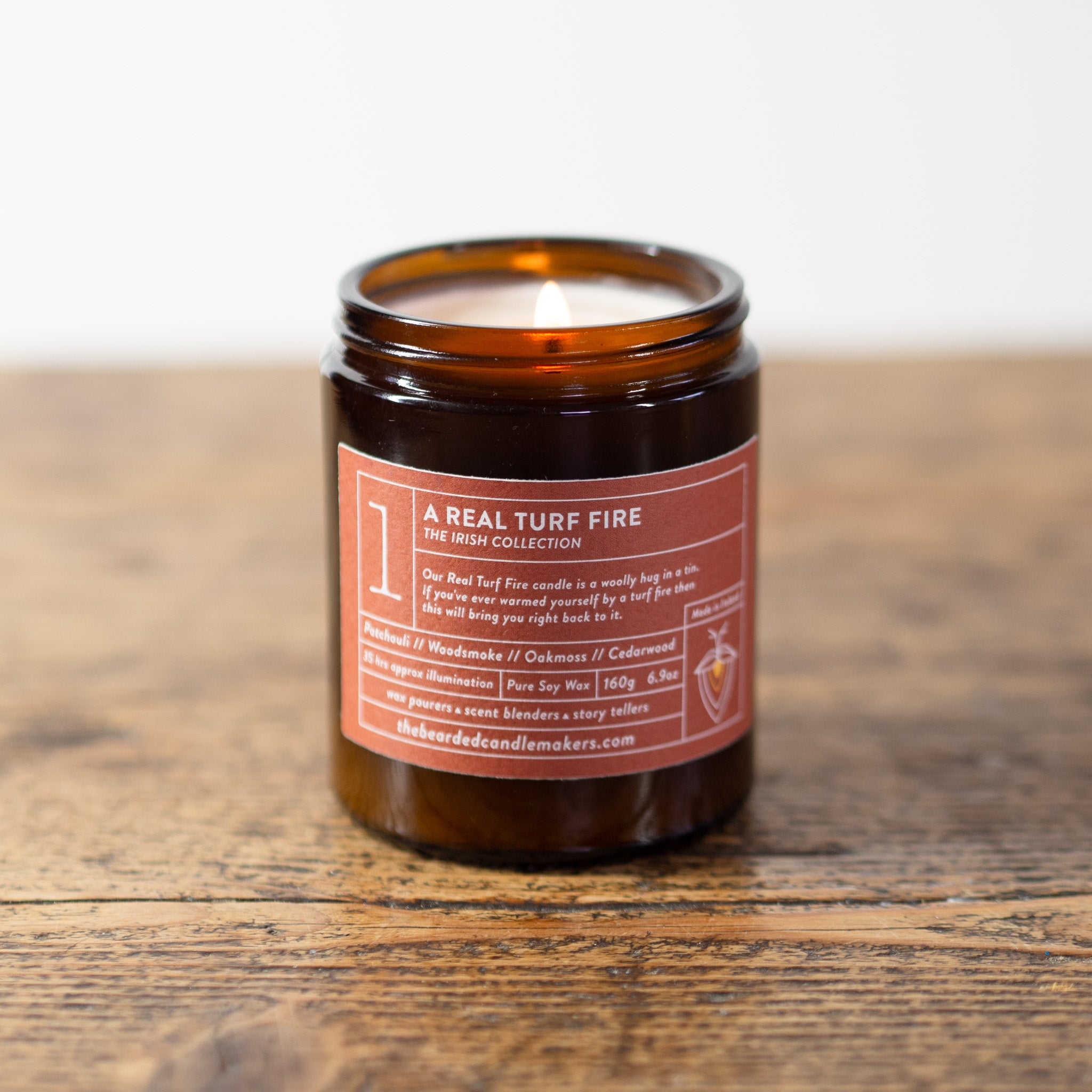 A photo of a candle called a Real Turf Fire on a wooden table.