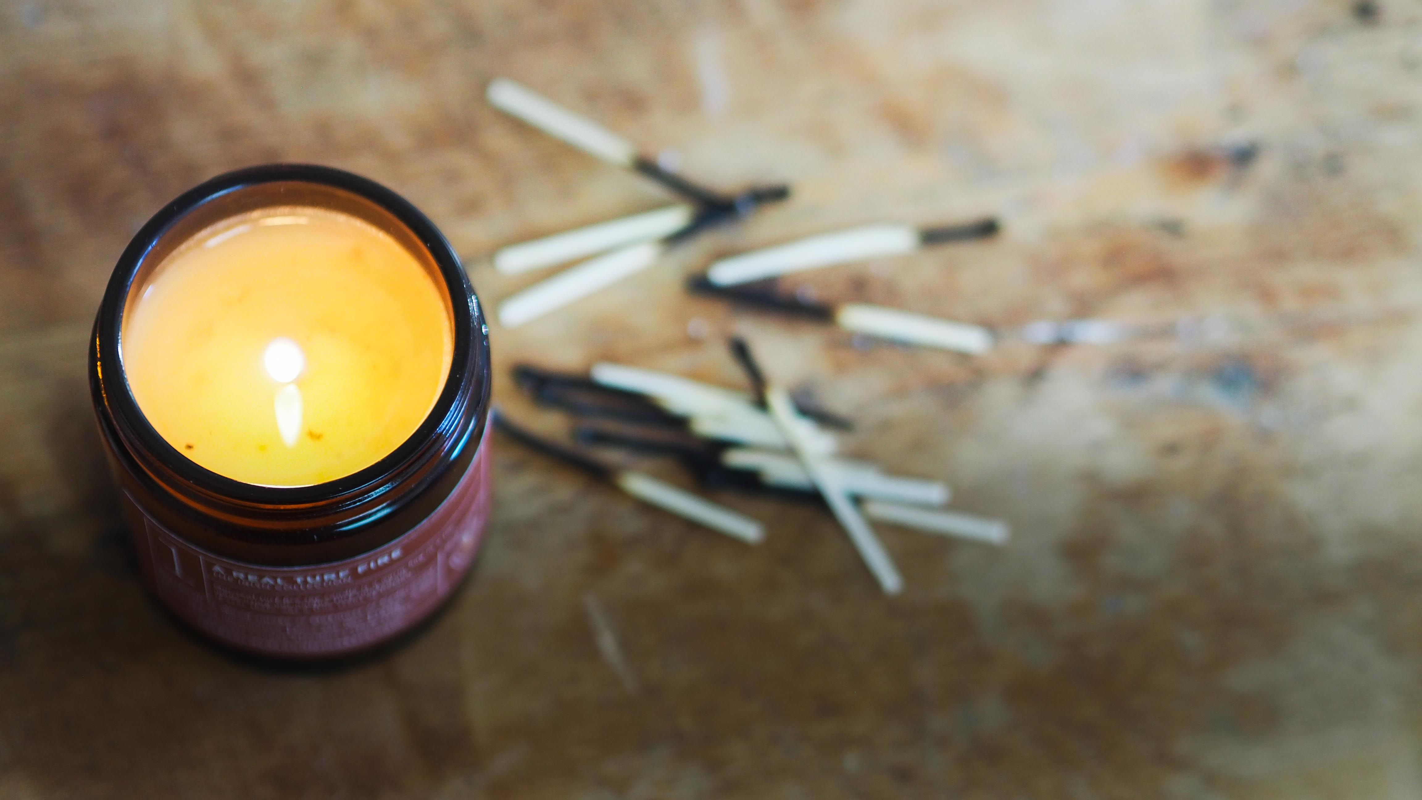 A Real Turf Fire soy candle, lit on a wooden table with a scattering of burnt matches