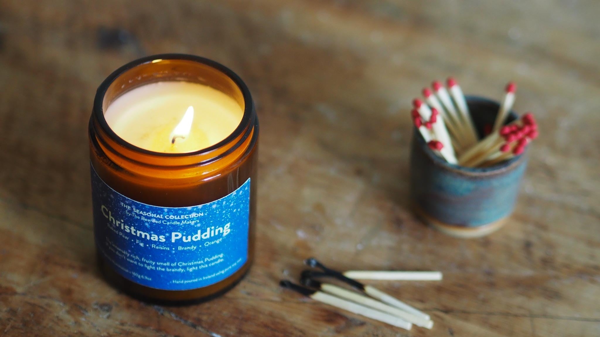 A Christmas Pudding lit candle on a table with matches around it. 