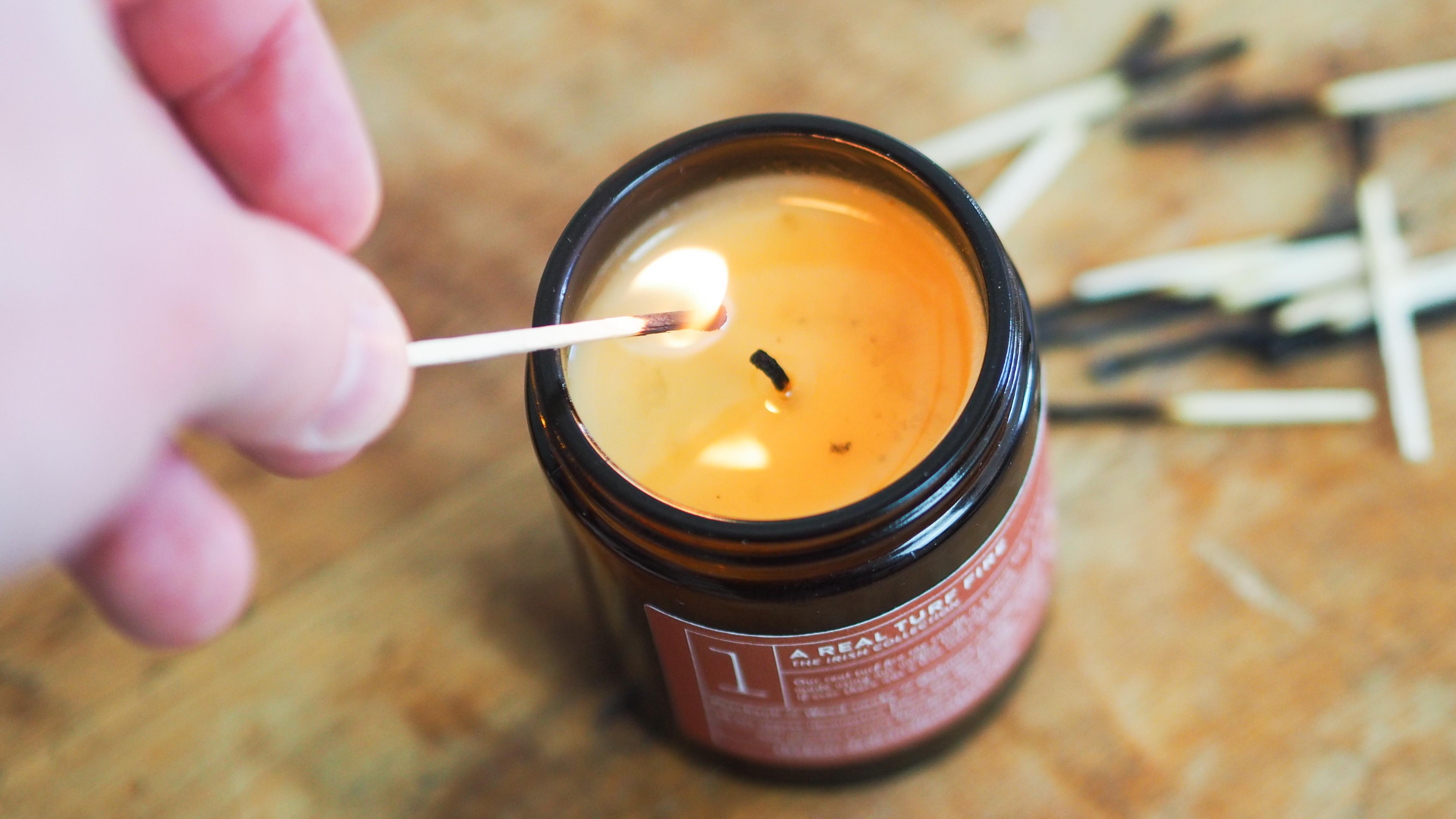 A lit candle with burnt match sticks behind sitting on a wooden table top.