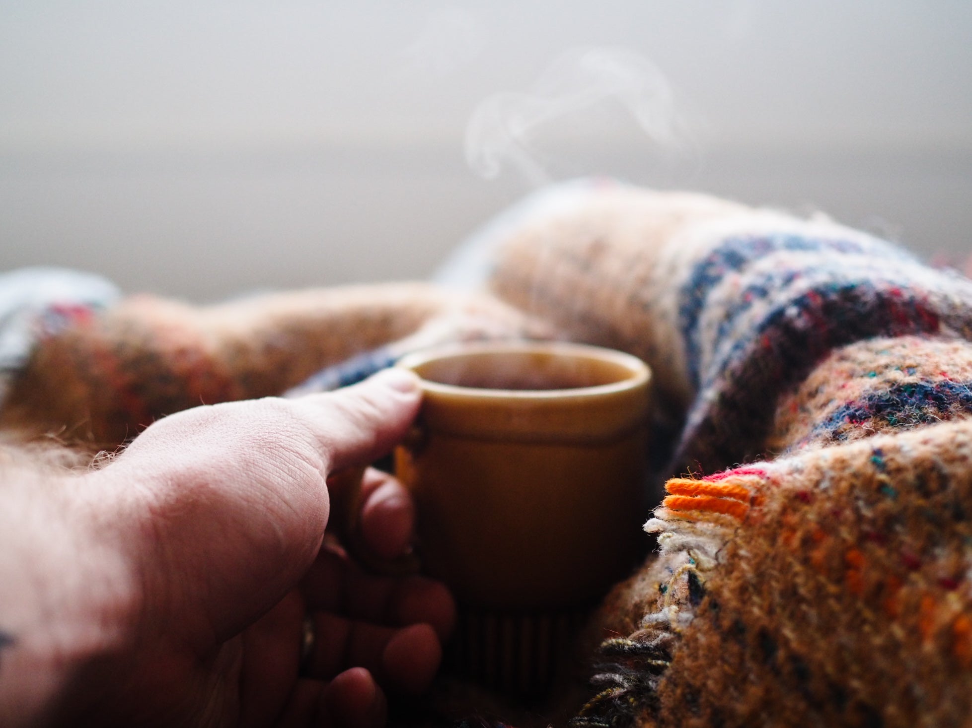 Michael holding a steaming cup of coffee with woollen blankets.