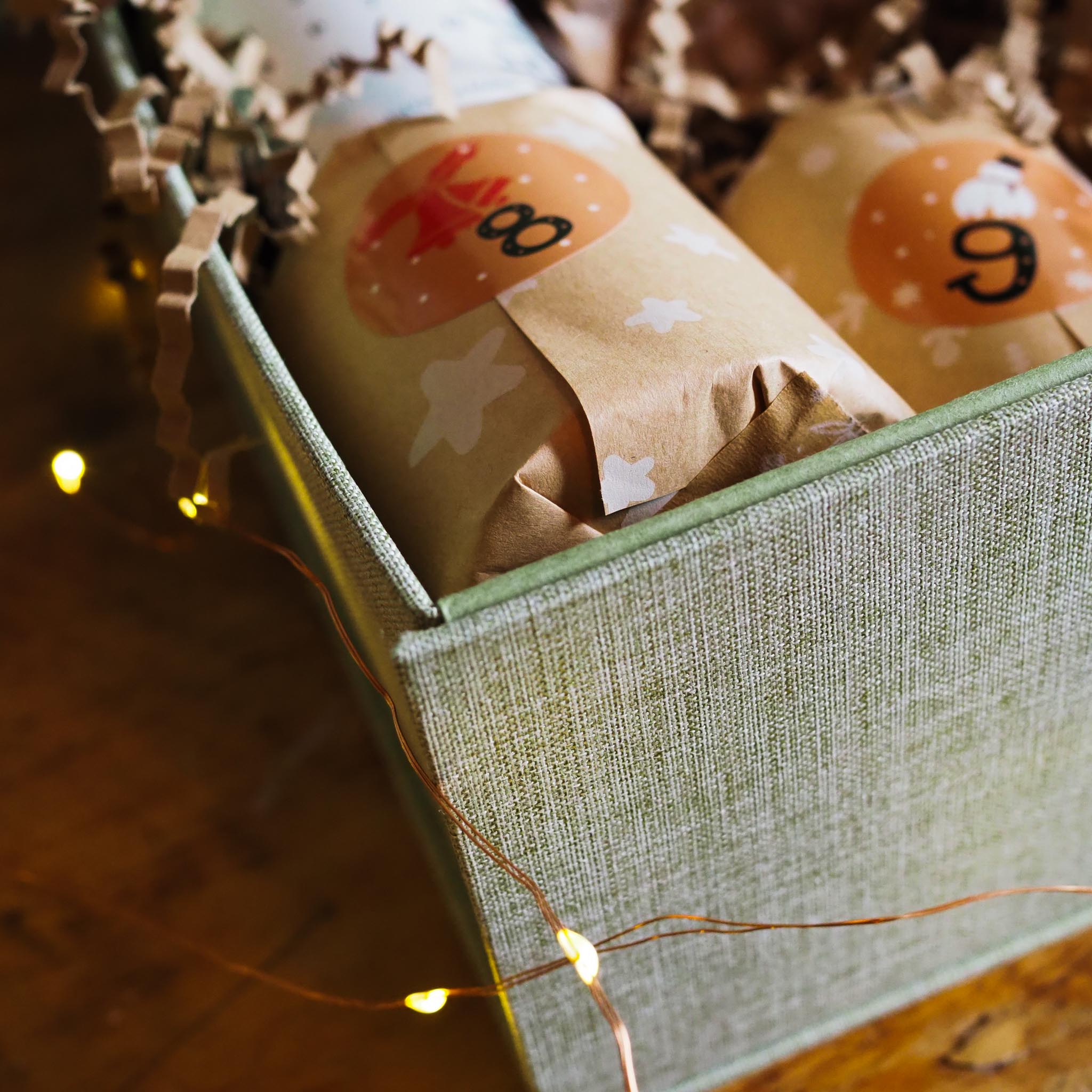 Gift wrapped in brown paper with white stars in a green box, surrounded by string lights.